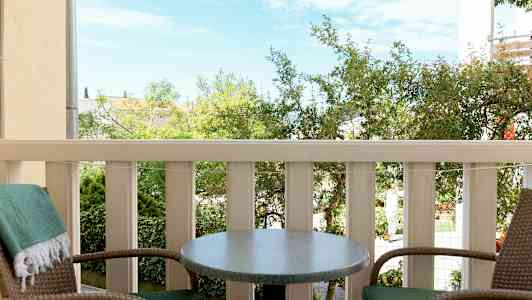 To stole og et bord på en altan med udsigt over et grønt område (AI-genereret tekst)