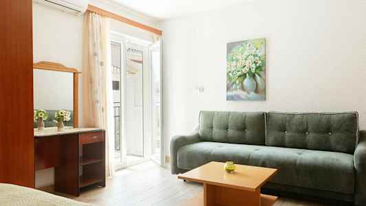 Et lyst interiør med en grøn sofa, et lille træbord og et spejl over et skrivebord. Et maleri af blomster hænger på væggen. (AI-genereret tekst)