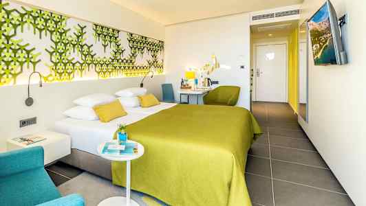 Et hotelværelse med en dobbeltseng med grønt sengetæppe og moderne møbler. (AI-genereret tekst)