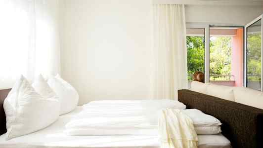 Et lyst rum med en seng tæt på vindue og altan. (AI-genereret tekst)