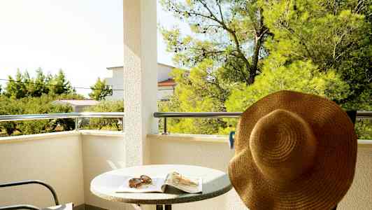 Altan med bord, stol og solhat, med udsigt til træer og bygninger. (AI-genereret tekst)