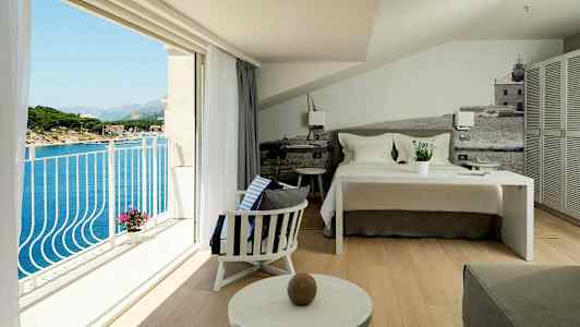 Et hotelværelse med en redt seng, siddeområde og en altan med udsigt over havet. (AI-genereret tekst)