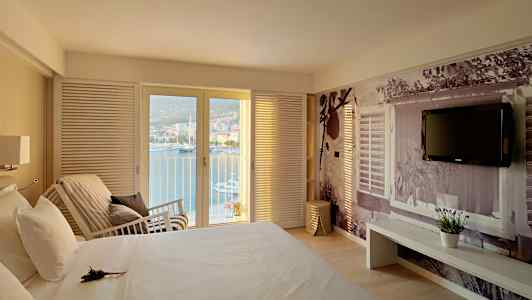 Soveværelse med udsigt over havet gennem glasdøre, en seng og en væg med dekorativ fotografi. (AI-genereret tekst)