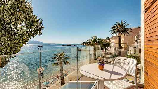 Udsigt fra en altan mod en solrig strand med palmer og klart vand. (AI-genereret tekst)