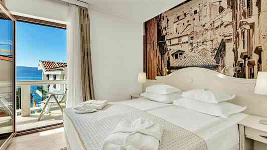 Et hotelværelse med en dobbeltseng, et bord og en glasdør, der leder til en altan med havudsigt. (AI-genereret tekst)