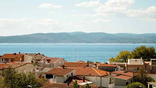 Røde tagene på huse med havet og bakker i baggrunden. (AI-genereret tekst)