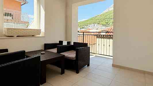 En terrasse med udsigt over tage og natur, møbleret med mørke rattanstole og bord. (AI-genereret tekst)