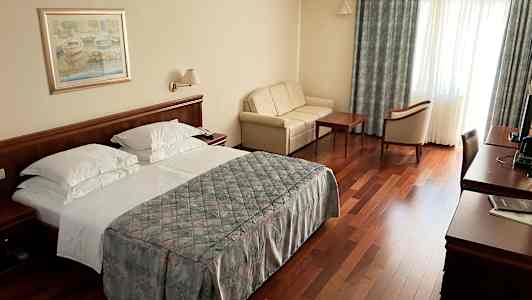 Et hotelværelse med en dobbeltseng, sofa, træbord og stole samt et skrivebord med tv. (AI-genereret tekst)