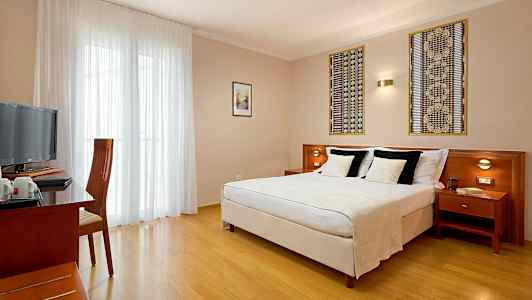 Et hotelværelse med en dobbeltseng, et skrivebord og en stol samt et fjernsyn. (AI-genereret tekst)