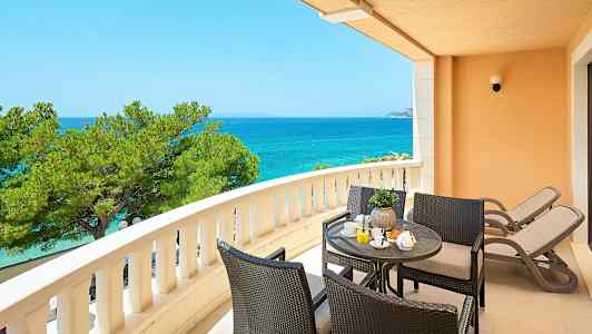 En balkon med udsigt over havet, siddegruppe og to liggestole. (AI-genereret tekst)