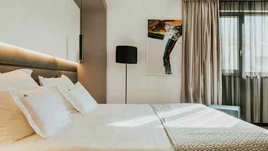 Moderne hotelværelse med en stor seng, kunstværk på væggen og et vindue med lyse gardiner. (AI-genereret tekst)