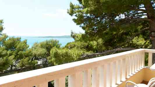 Udsigt fra en altan med hvide rækværk mod træer og hav. (AI-genereret tekst)