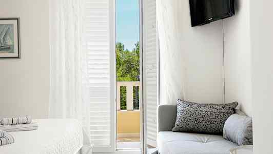 Et hotelværelse med en sofa, en seng og en altandør, der fører ud til udsigt over træer. (AI-genereret tekst)