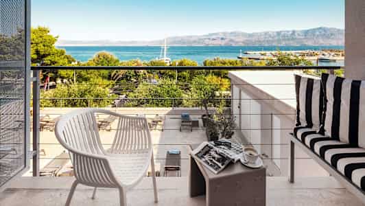 Udsigt fra en terrasse med møbler, med udsigt til havet og bjergene. (AI-genereret tekst)