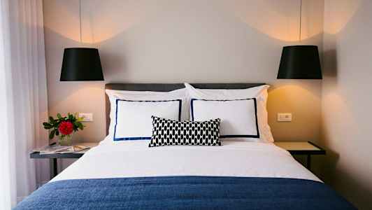 Billede af en redt seng med dekorative puder og hængende lamper. (AI-genereret tekst)