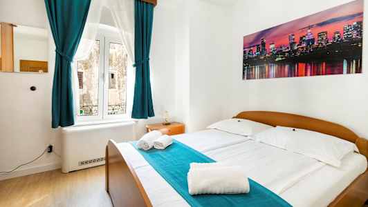 Et soveværelse med dobbeltseng, turkise gardiner og et billede af en bysilhuet på væggen. (AI-genereret tekst)