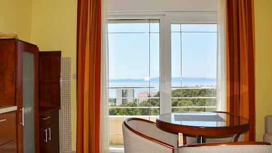 Et værelse med store vinduer, der vender ud mod en havudsigt, med møbler inklusive et rundt bord og stole. (AI-genereret tekst)