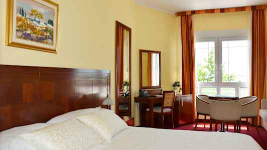 Et hotelværelse med en dobbeltseng, skrivebord, stole og et vindue. (AI-genereret tekst)