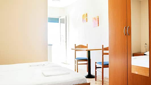 Et hotelværelse med to enkeltsenge, et bord med to stole og et klædeskab. (AI-genereret tekst)