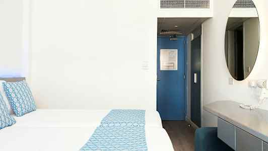 Hotelværelse med to senge, blå detaljer og skrivebord. (AI-genereret tekst)