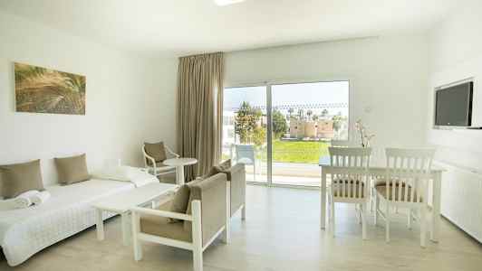 Lyst møbleret værelse med seng, stole, bord og udsigt til grønt område gennem store vinduer. (AI-genereret tekst)