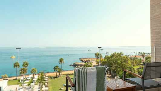 Udsigt fra en balkon over havet med både og en strand med palmer. (AI-genereret tekst)