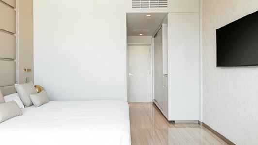 Et moderne hotelværelse med en stor seng, hvid væg, en dør og et vægmonteret TV. (AI-genereret tekst)