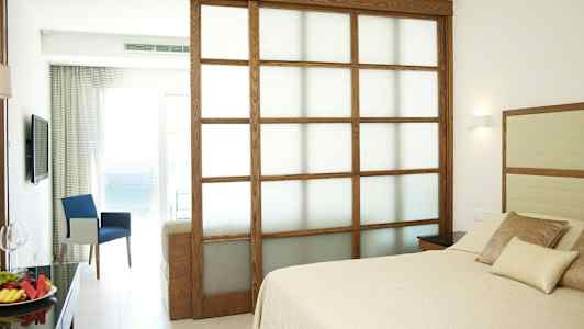 Hotelværelse med seng og siddegruppe samt udsigt til havet. (AI-genereret tekst)