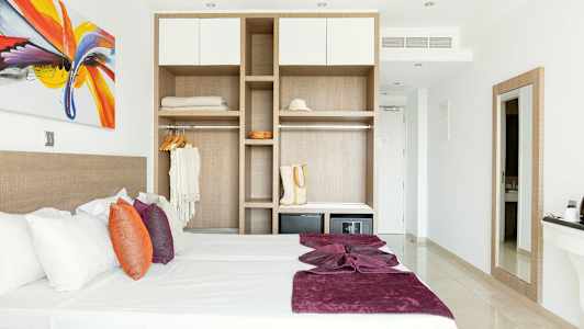 Moderne indrettet hotelværelse med seng, farverige puder og åben garderobe. (AI-genereret tekst)