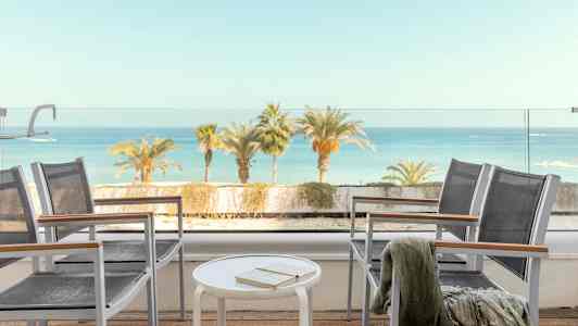 Udsigt fra en terrasse med stole, bord og havet i baggrunden. (AI-genereret tekst)