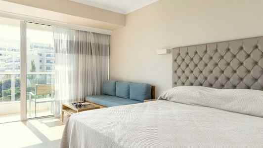 Et hotelværelse med en seng, en blå sofa og en altan. (AI-genereret tekst)