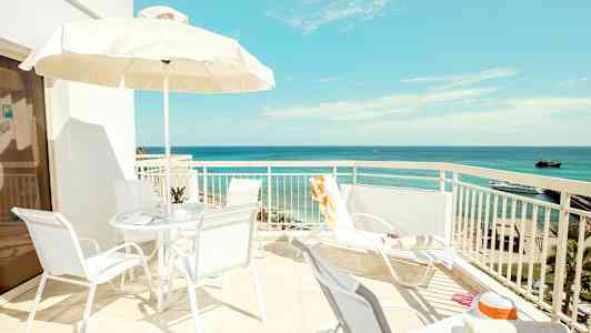 En solrig terrasse med udsigt over havet, stole og parasol. (AI-genereret tekst)