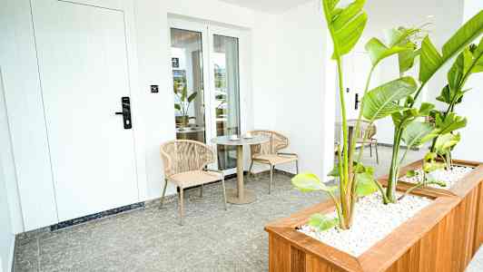 En terrasse med to stole og et bord, omgivet af grønne planter. (AI-genereret tekst)