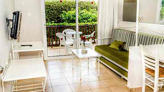 En stue med en grøn sofa, hvidt bord og stole samt en balkon med havemøbler. (AI-genereret tekst)