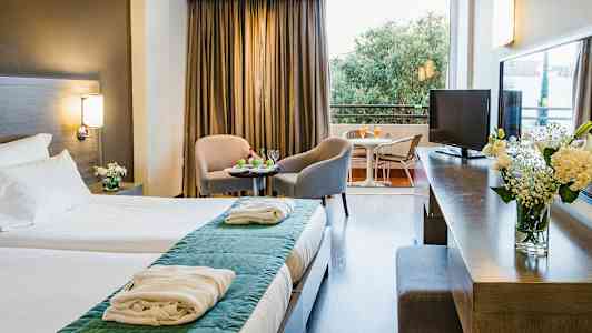 Et hotelværelse med dobbeltseng, siddegruppe med to stole og bord samt en balkon med udsigt. (AI-genereret tekst)