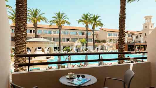 Udsigt fra en balkon til en pool og omkringliggende hotelbygninger. (AI-genereret tekst)