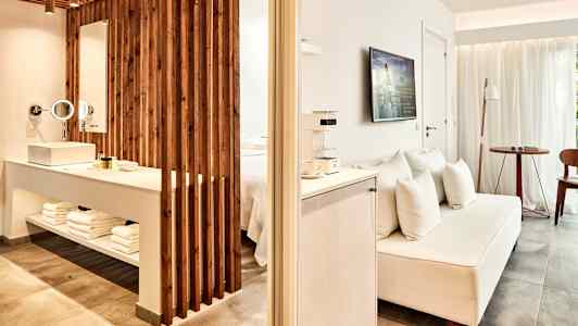 Et hotelværelse med åben planløsning, inklusive en TV, en sofa og et område med håndvask og badeartikler. (AI-genereret tekst)