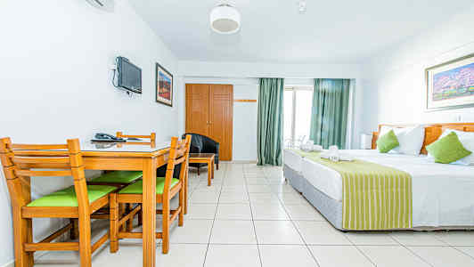 Et hotelværelse med en seng, et spisebord med stole og et vægmonteret TV. (AI-genereret tekst)