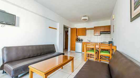 Et interiør med to brune sofaer, et glasbord og et køkkenområde med trærkeskabe og spiseplads. (AI-genereret tekst)