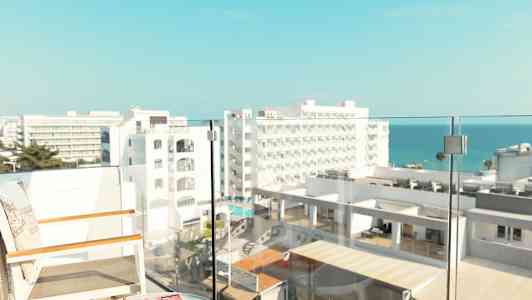 Udsigt fra en altan med stole og et bord, med hotelbygninger og havet i baggrunden. (AI-genereret tekst)