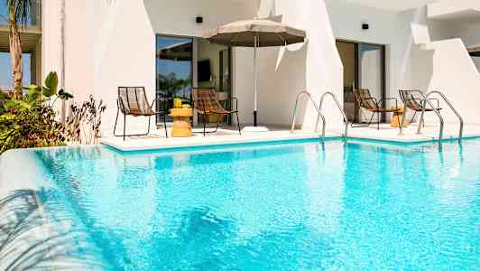 En udendørs pool foran en bygning med borde og stole i baggrunden. (AI-genereret tekst)