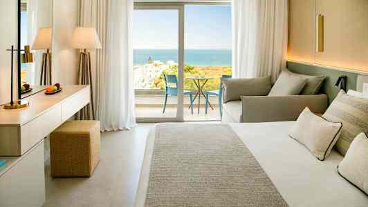 Et hotelværelse med en dobbeltseng, siddeområde og en balkon med udsigt over havet. (AI-genereret tekst)