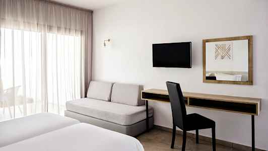 Et hotelværelse med to senge, en sofa, et skrivebord og et vægmonteret TV. (AI-genereret tekst)