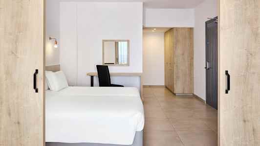 Et hotelværelse med en dobbeltseng, skrivebord, spejl og opbevaringsmøbler. (AI-genereret tekst)