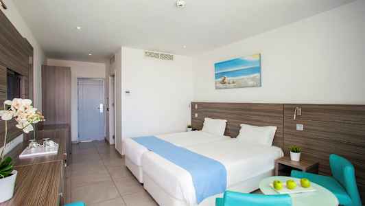 Hotelværelse med to senge, et bord og stole. (AI-genereret tekst)