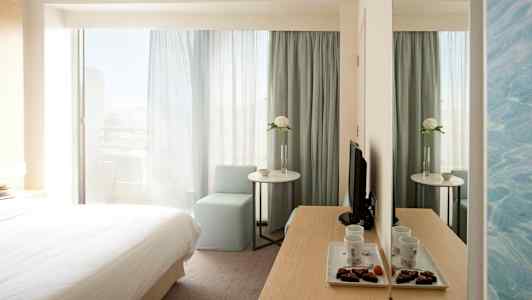 Hotelværelse med seng, bord, stol og spejl. (AI-genereret tekst)