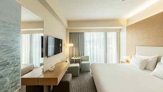 Hotelværelse med en stor seng, TV på væggen og siddegruppe ved vinduet. (AI-genereret tekst)