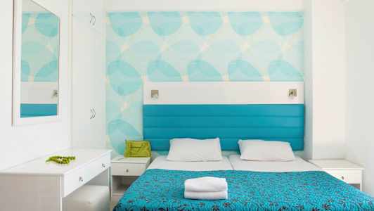 Et hotelværelse med to senge, blå betræk og hvidt interiør. (AI-genereret tekst)