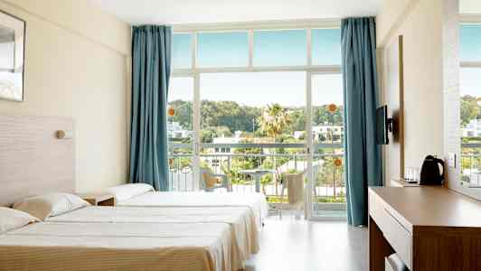 Et hotelværelse med to senge, blå gardiner og en altan med udsigt over grønne omgivelser. (AI-genereret tekst)