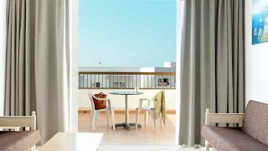 Et hotelværelse med udsigt til en altan med et bord og stole. (AI-genereret tekst)